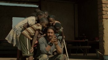 Movie still from “Machine Gun Preacher” (2011), directed by Marc Forster – A group of children standing next to a man holding a cell phone; Wide shot, Low angle