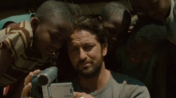 Movie still from “Machine Gun Preacher” (2011), directed by Marc Forster – A man holding a video camera in front of a group of children; Close Up shot, High angle