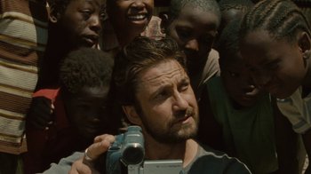 Movie still from “Machine Gun Preacher” (2011), directed by Marc Forster – A man holding a video camera in front of a group of people; Close Up shot, High angle