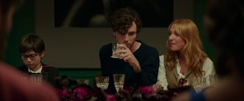 Movie still from “Madame” (2017), directed by Amanda Sthers – A man holding a glass of water while sitting at a table; Medium shot, Over the shoulder angle