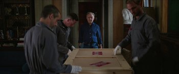 Movie still from “Madame” (2017), directed by Amanda Sthers – A group of people standing around a wooden box; Medium shot, Over the shoulder angle