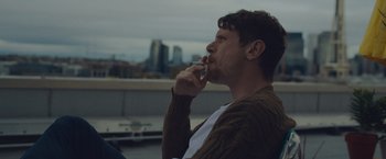 Movie still from “Little Fish” (2020), directed by Chad Hartigan – A man sitting on the ground smoking a cigarette; Close Up shot, Low angle
