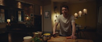 Movie still from “Little Fish” (2020), directed by Chad Hartigan – A man standing in front of a counter with a knife; Medium shot, Over the shoulder angle