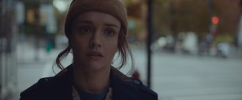 Movie still from “Little Fish” (2020), directed by Chad Hartigan – A young woman wearing a hat and looking at the camera; Close Up shot, Over the shoulder angle
