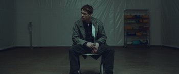 Movie still from “Little Fish” (2020), directed by Chad Hartigan – A man sitting on top of a metal chair; Medium shot, High angle