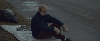 Movie still from “Little Fish” (2020), directed by Chad Hartigan – A man sitting on the ground with his mouth taped shut; Medium shot, High angle