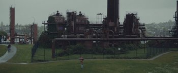 Movie still from “Little Fish” (2020), directed by Chad Hartigan – A person holding an umbrella while standing in front of a factory; Extreme Wide shot, High angle