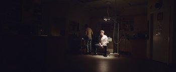 Movie still from “Little Fish” (2020), directed by Chad Hartigan – A man sitting on a chair in a room; Wide shot, Low angle