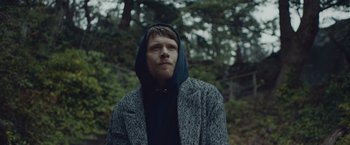 Movie still from “Little Fish” (2020), directed by Chad Hartigan – A man in a hooded jacket standing in the woods; Close Up shot, Low angle