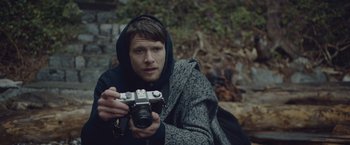 Movie still from “Little Fish” (2020), directed by Chad Hartigan – A man holding a camera while sitting on the ground; Close Up shot, Low angle