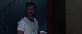 Movie still from “Malignant” (2021), directed by James Wan – A man standing in a dark room next to a wooden wall; Medium shot, Over the shoulder angle