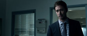 Movie still from “Malignant” (2021), directed by James Wan – A man in a suit standing in front of a window; Close Up shot, Over the shoulder angle