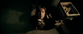 Movie still from “Malignant” (2021), directed by James Wan – A woman is looking up at the camera; Medium shot, Overhead angle
