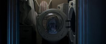 Movie still from “Malignant” (2021), directed by James Wan – A woman is in a washing machine with a reflection of herself in it; Medium shot, Low angle
