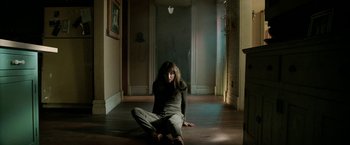 Movie still from “Malignant” (2021), directed by James Wan – A woman sitting on the ground in a room; Wide shot, High angle