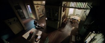 Movie still from “Malignant” (2021), directed by James Wan – A woman sitting on the floor of a living room next to a table; Extreme Wide shot, High angle