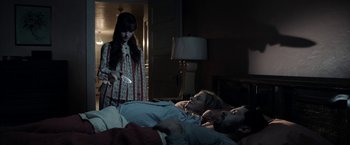 Movie still from “Malignant” (2021), directed by James Wan – A woman standing next to a man laying in a bed; Medium shot, High angle