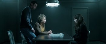 Movie still from “Malignant” (2021), directed by James Wan – A woman sitting at a table in a dark room; Medium shot, Over the shoulder angle