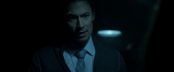 Movie still from “Malignant” (2021), directed by James Wan – A man wearing a suit and tie in a dark room; Close Up shot, Low angle