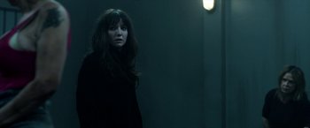Movie still from “Malignant” (2021), directed by James Wan – A woman standing in a dark room next to a light; Medium shot, Over the shoulder angle