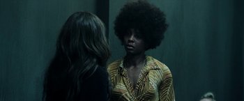 Movie still from “Malignant” (2021), directed by James Wan – A woman in a yellow and black shirt is talking to another woman in front of a mirror; Close Up shot, Over the shoulder angle