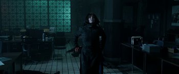 Movie still from “Malignant” (2021), directed by James Wan – A woman standing in a dark room holding a gun; Medium shot, Over the shoulder angle