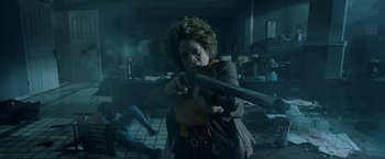 Movie still from “Malignant” (2021), directed by James Wan – A woman is holding a gun in a room; Medium shot, High angle