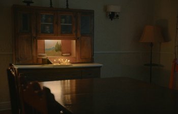 Movie still from “Marcel the Shell with Shoes On” (2021), directed by Dean Fleischer Camp – Candles are lit on a table in front of a lighted cabinet; Wide shot, High angle