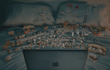 Movie still from “Marcel the Shell with Shoes On” (2021), directed by Dean Fleischer Camp – An apple computer sitting on top of a bed covered in toys; Wide shot, Overhead angle