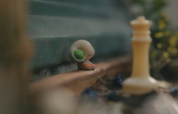 Movie still from “Marcel the Shell with Shoes On” (2021), directed by Dean Fleischer Camp – A toy snail sitting next to a chess piece on the ground; Extreme Close Up shot, High angle