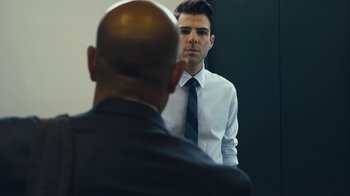 Movie still from “Margin Call” (2011), directed by J.C. Chandor – A man in a suit and tie looking at himself in the mirror; Medium shot, Over the shoulder angle