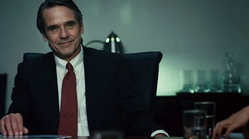 Movie still from “Margin Call” (2011), directed by J.C. Chandor – A man sitting at a table in a suit and tie; Close Up shot, Over the shoulder angle