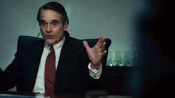 Movie still from “Margin Call” (2011), directed by J.C. Chandor – A man sitting at a table in front of a wall; Close Up shot, Over the shoulder angle