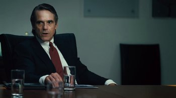 Movie still from “Margin Call” (2011), directed by J.C. Chandor – A man in a suit and tie sitting at a table; Medium shot, Over the shoulder angle