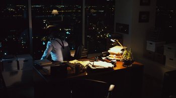 Movie still from “Margin Call” (2011), directed by J.C. Chandor – A person standing in front of a desk with papers on top of it; Wide shot, High angle