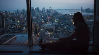 Movie still from “Margin Call” (2011), directed by J.C. Chandor – A woman sitting on the ground looking out of a window at night; Medium shot, High angle