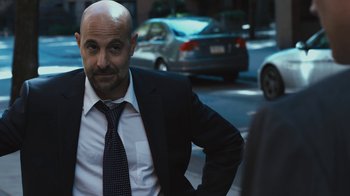 Movie still from “Margin Call” (2011), directed by J.C. Chandor – A man in a suit and tie standing in front of a car; Medium shot, Over the shoulder angle