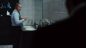 Movie still from “Margin Call” (2011), directed by J.C. Chandor – A man standing in front of a bathroom mirror; Medium shot, Over the shoulder angle