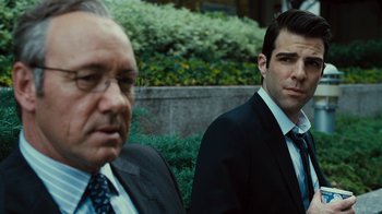 Movie still from “Margin Call” (2011), directed by J.C. Chandor – A man in a suit and tie standing next to another man in a suit and tie; Close Up shot, Over the shoulder angle