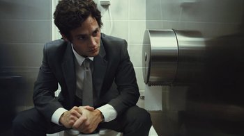 Movie still from “Margin Call” (2011), directed by J.C. Chandor – A man in a suit sitting in front of a urinal; Medium shot, Low angle
