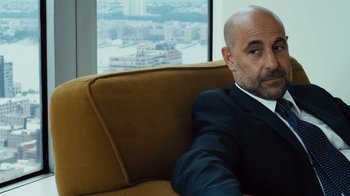 Movie still from “Margin Call” (2011), directed by J.C. Chandor – A man in a suit sitting on top of a brown couch; Close Up shot, Over the shoulder angle