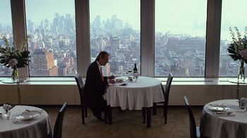 Movie still from “Margin Call” (2011), directed by J.C. Chandor – A man sitting at a dinner table in front of a large window; Wide shot, High angle