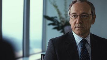 Movie still from “Margin Call” (2011), directed by J.C. Chandor – A man in a suit and tie sitting in a chair; Close Up shot, Over the shoulder angle