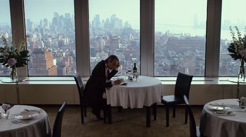 Movie still from “Margin Call” (2011), directed by J.C. Chandor – A man sitting at a table with a bottle of wine; Wide shot, High angle