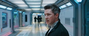 Movie still from “Maze Runner: The Death Cure” (2018), directed by Wes Ball – A man standing in a hallway with people in the background; Close Up shot, Over the shoulder angle