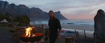 Movie still from “Maze Runner: The Death Cure” (2018), directed by Wes Ball – A man standing next to an open fire on the beach; Wide shot, Over the shoulder angle