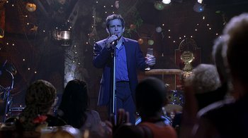 Movie still from “Meet the Fockers” (2004), directed by Jay Roach – A man in a blue suit is holding a microphone; Medium shot, Over the shoulder angle
