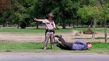 Movie still from “Meet the Fockers” (2004), directed by Jay Roach – A man in a brown jacket and a brown hat pointing a gun at a man laying on the ground; Wide shot, Low angle