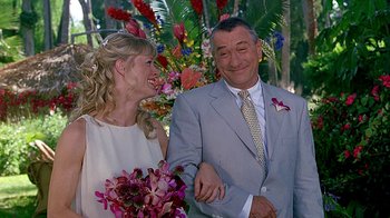 Movie still from “Meet the Fockers” (2004), directed by Jay Roach – A man and a woman smile at each other while standing next to each other in front of flowers; Medium shot, Over the shoulder angle
