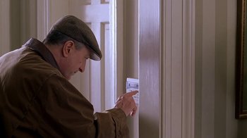 Movie still from “Meet the Parents” (2000), directed by Jay Roach – A man in brown jacket and hat looking at a button on a white door; Medium shot, Low angle